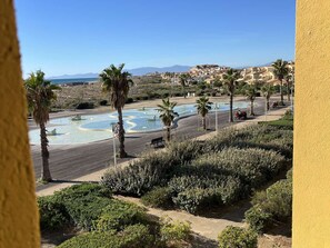 A landscaped area with a pool, palm trees, and a view of a coastal town. - Duplex with panoramic view - 4 guests (Port Leucate)