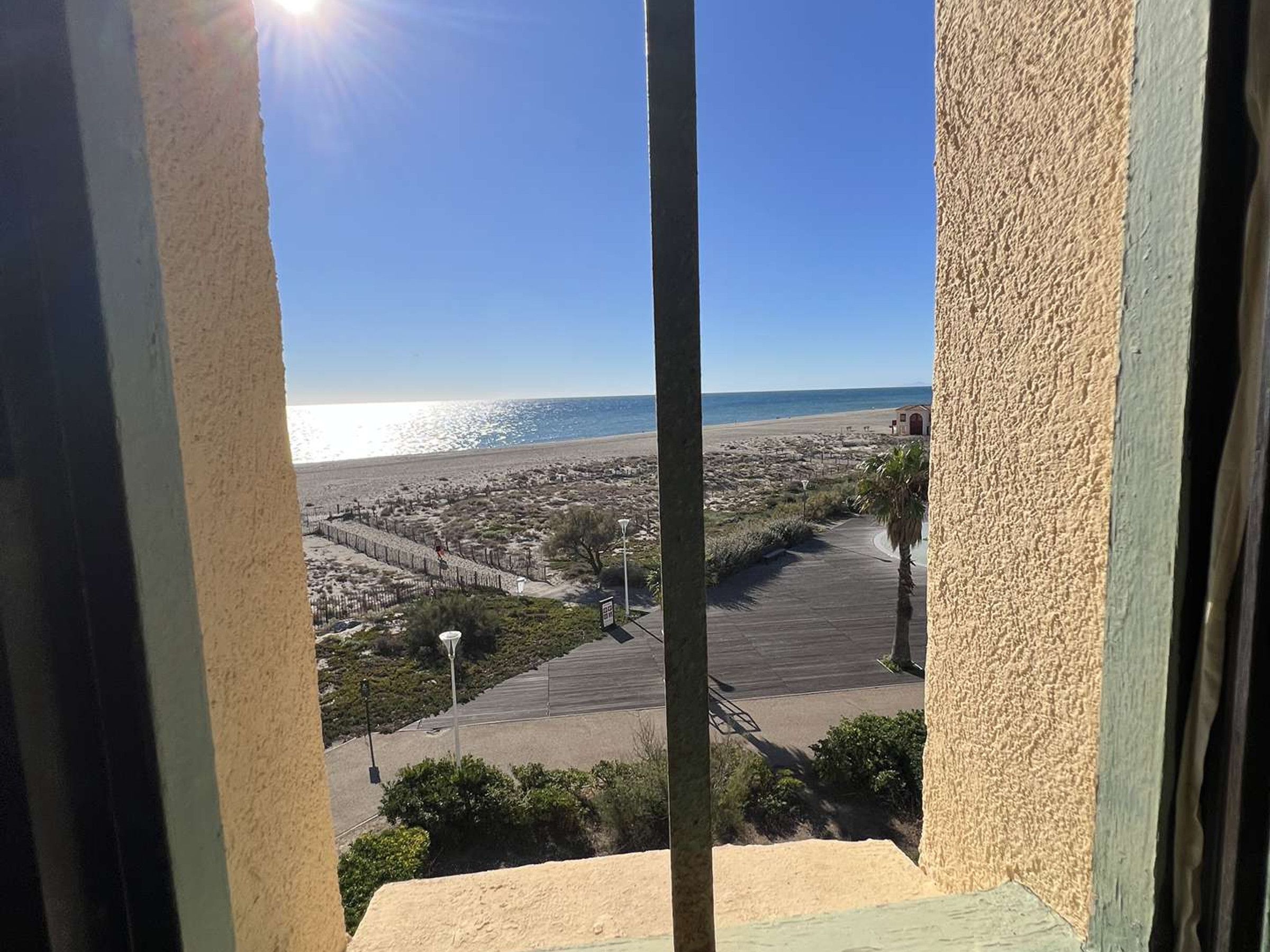 A coastal view from a balcony with a clear sky, a beach, and a small building.