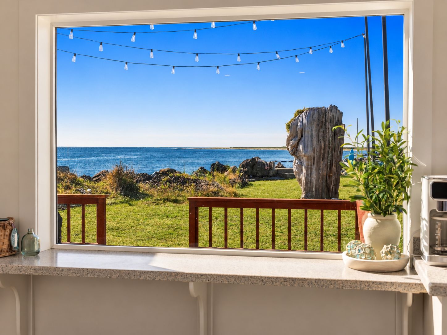 A kitchen with a large window overlooking a rocky coastline, a wooden bench, and a potted plant.