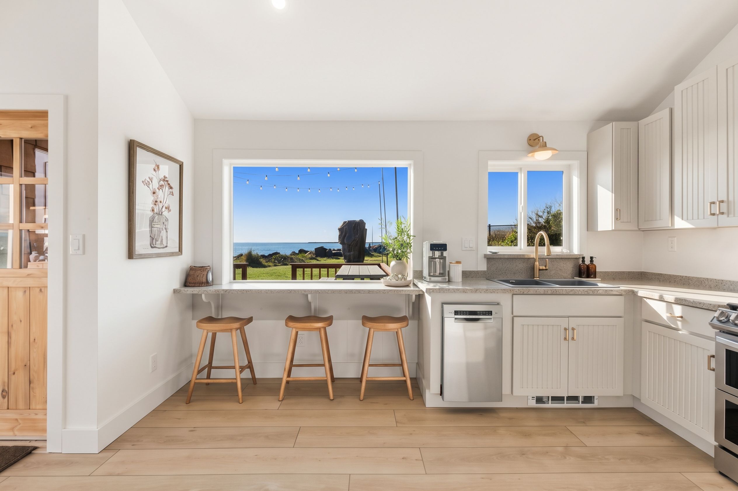 Une cuisine moderne dotée d’une grande fenêtre offrant une vue panoramique, de tabourets en bois et d’un lave-vaisselle encastré.