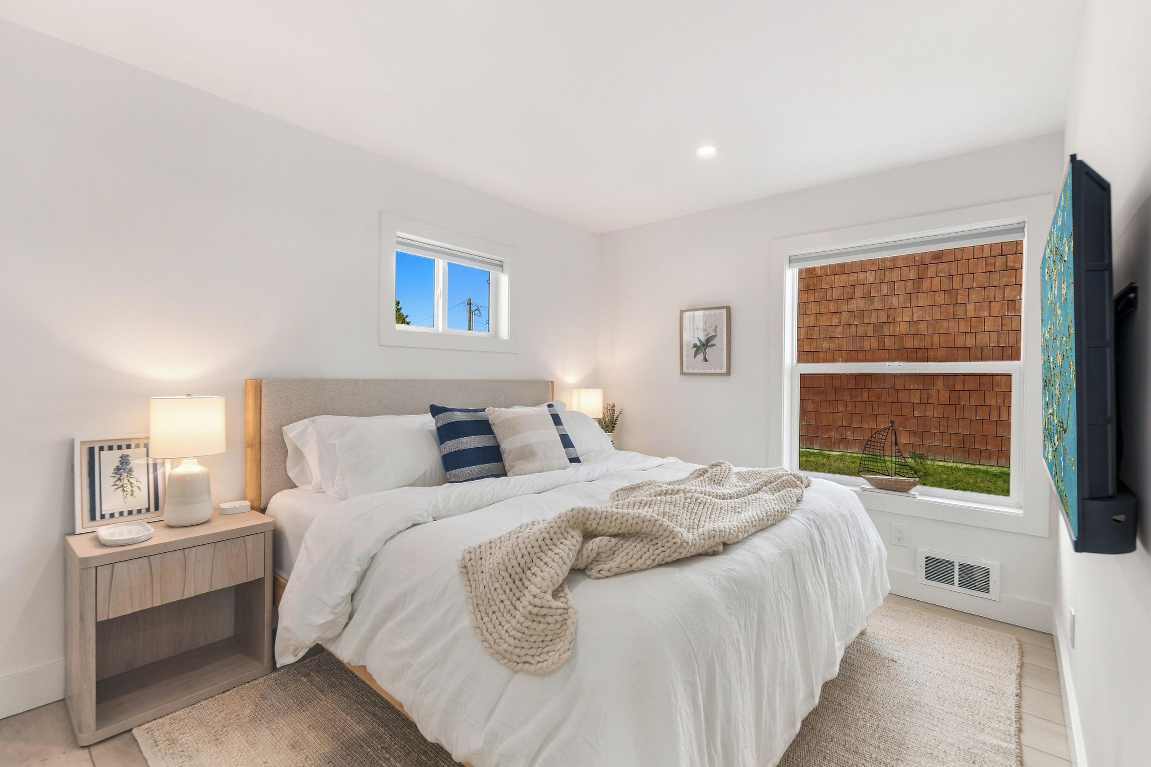 Une chambre à coucher avec un lit, des tables de chevet, une fenêtre donnant sur un beau paysage et un téléviseur fixé au mur.