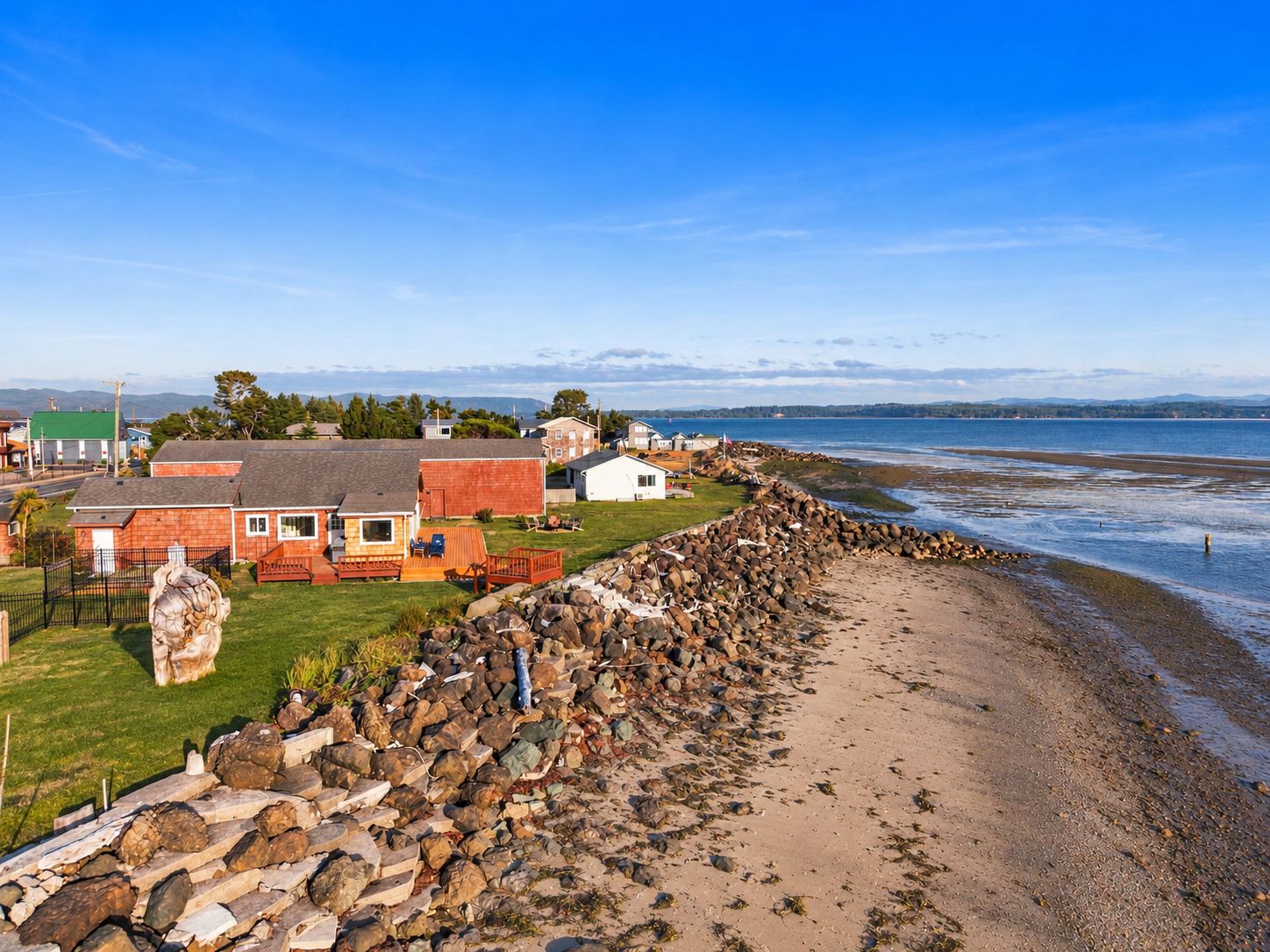 A coastal residential area with houses, a rocky breakwater, and a clear view of the sea.