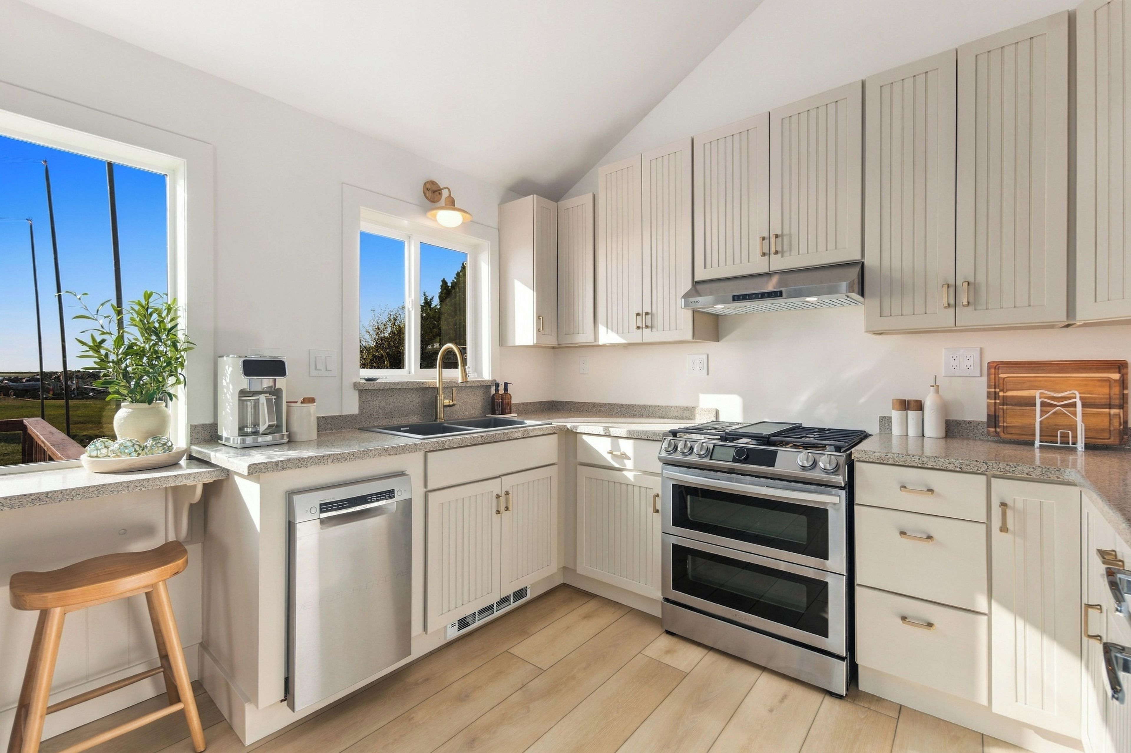 A modern kitchen with white cabinetry, stainless steel appliances, and a large window providing a view of the outdoors.