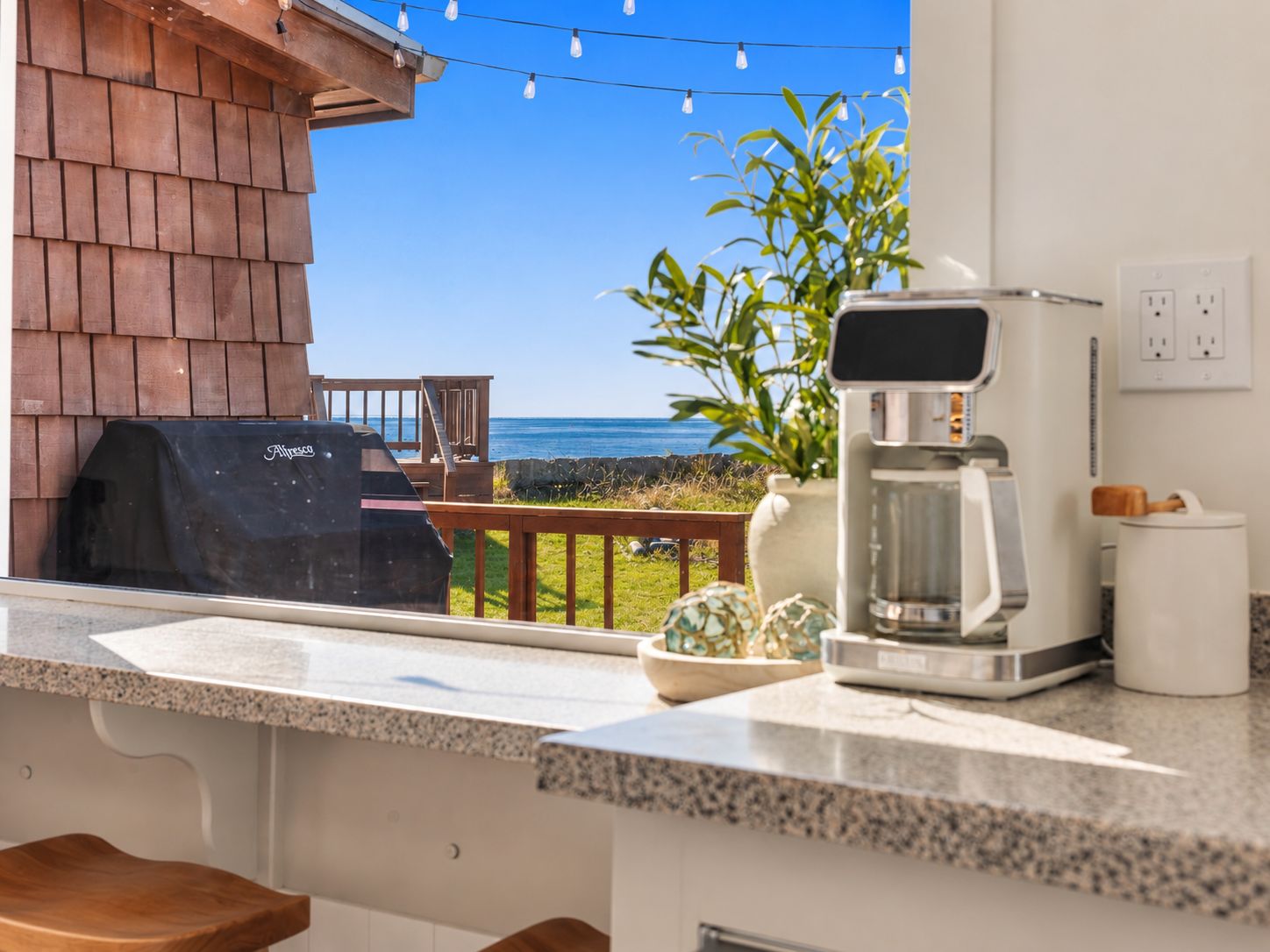 A kitchen with a coffee maker, a grill, and a view of the ocean.