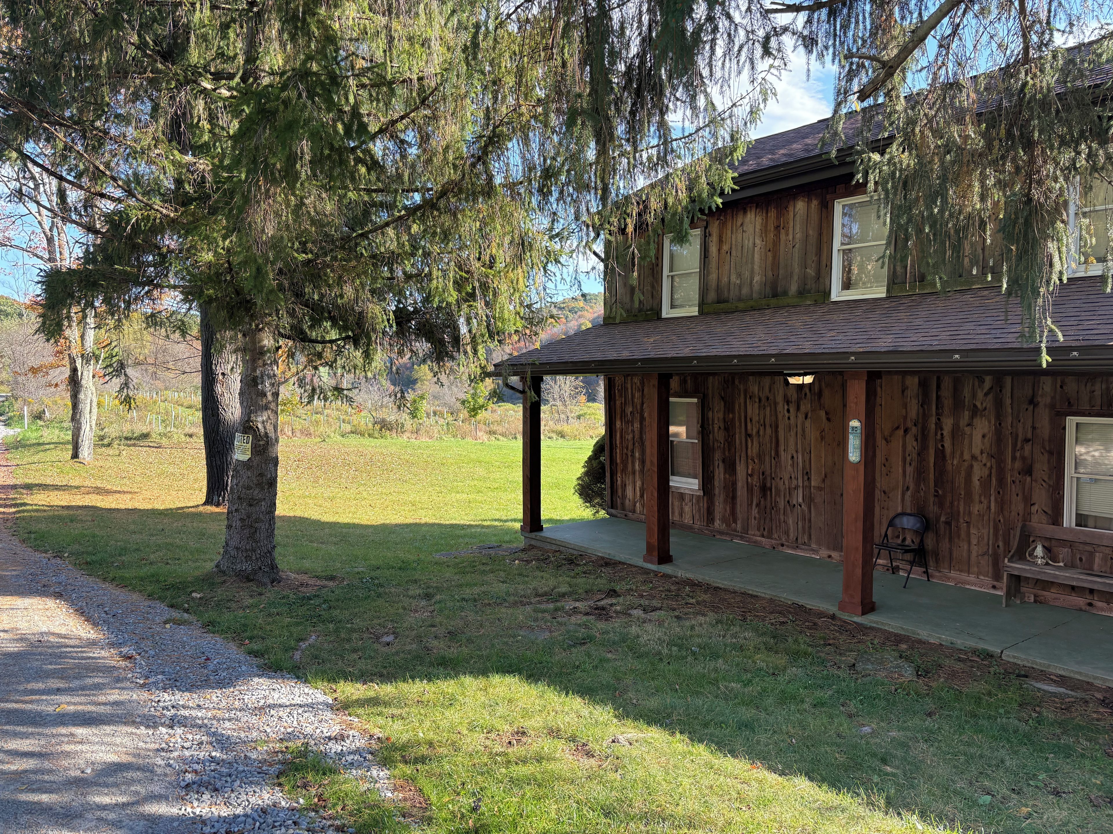A rustic wooden building with a porch, a gravel path, and a grassy area.