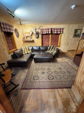 A cozy living room with a leather sectional sofa, a patterned rug, wooden flooring, and a deer head mounted on the wall.