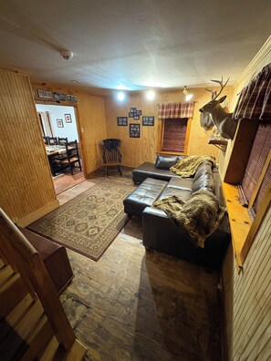 A cozy living room with a leather sofa, a patterned rug, and a mounted deer head on the wall. - Cozy, Tranquil Cabin close to Breweries, Flight 93, Seven Springs,Hidden Valley. (Fairhope)