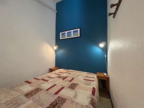 A bedroom with a blue wall, a quilted bedspread, two bedside tables, and two wall-mounted lamps. - House with AC, pool, pets welcome - 6 guests (Fleury-Saint-Pierre-la-Mer)