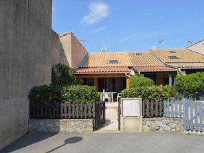 A residential building with a tiled roof, a gated entrance, and a small outdoor seating area. - House with AC, pool, pets welcome - 6 guests (Fleury-Saint-Pierre-la-Mer)