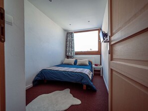 Ein Schlafzimmer mit einem Bett, einem Fenster, einer Heizung und einem weißen Teppich.