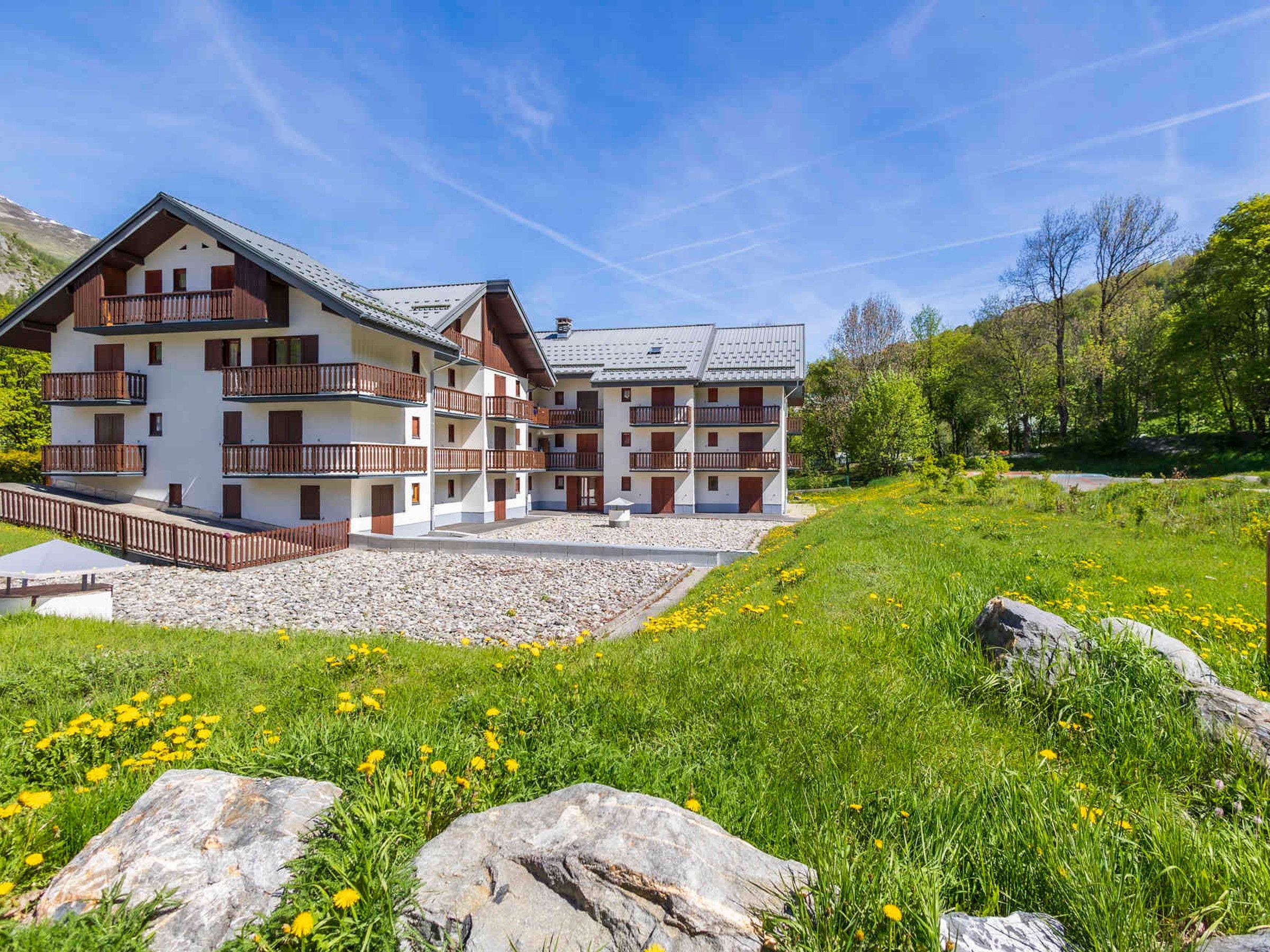 A multi-story building with balconies, set in a natural landscape with grass and rocks.