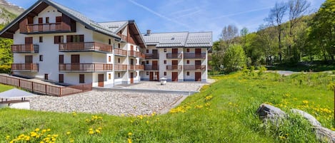 A multi-story building with balconies, set in a natural landscape with grass and rocks.