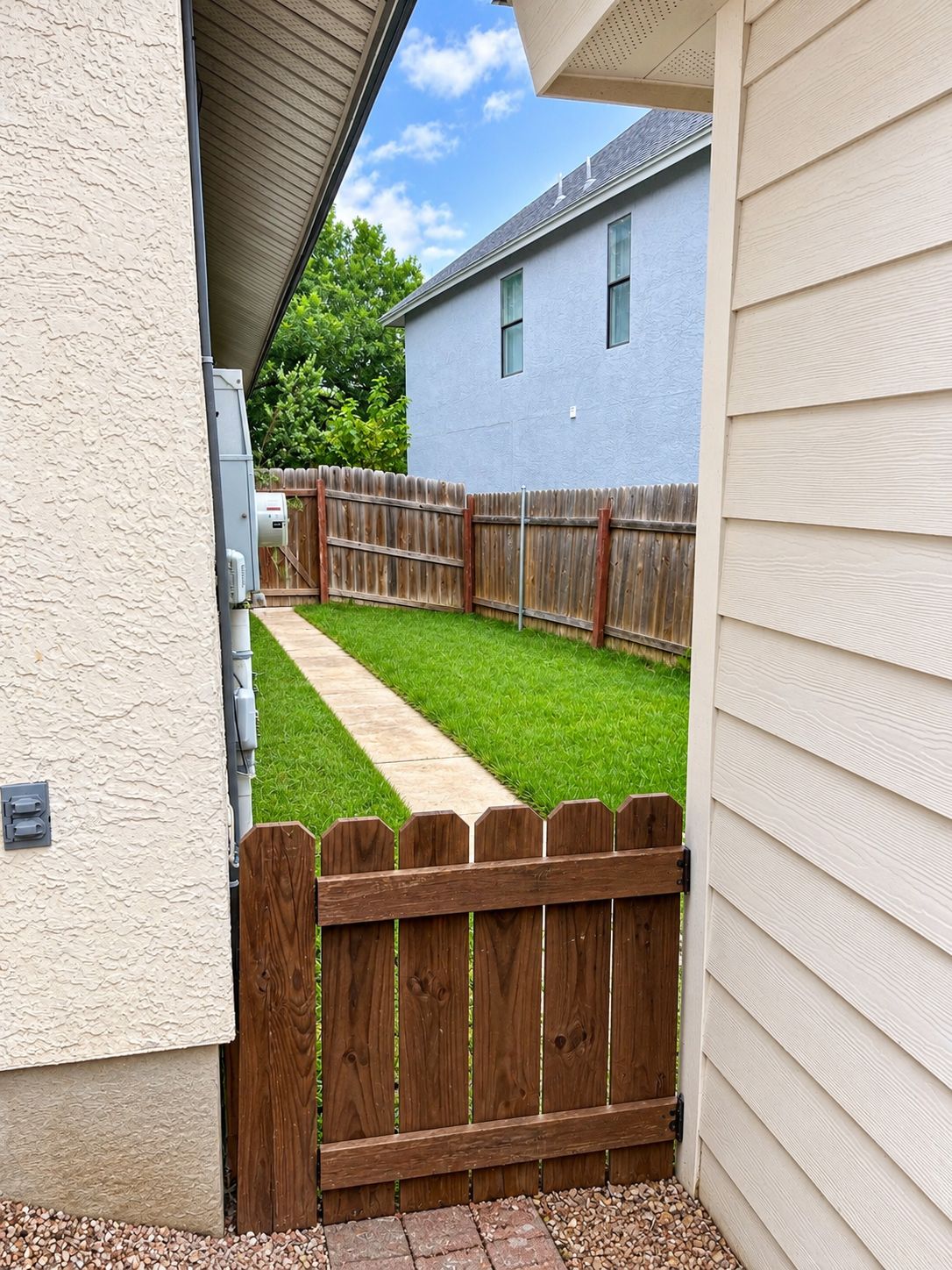 Un jardin avec une clôture en bois, un chemin et une maison bleue en arrière-plan.