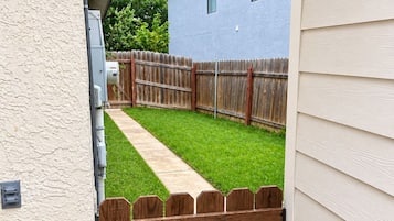 Un jardin avec une clôture en bois, un chemin et une maison bleue en arrière-plan.
