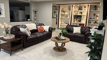 Un salon moderne avec un canapé en cuir marron, une table basse et une bibliothèque remplie d’objets décoratifs.