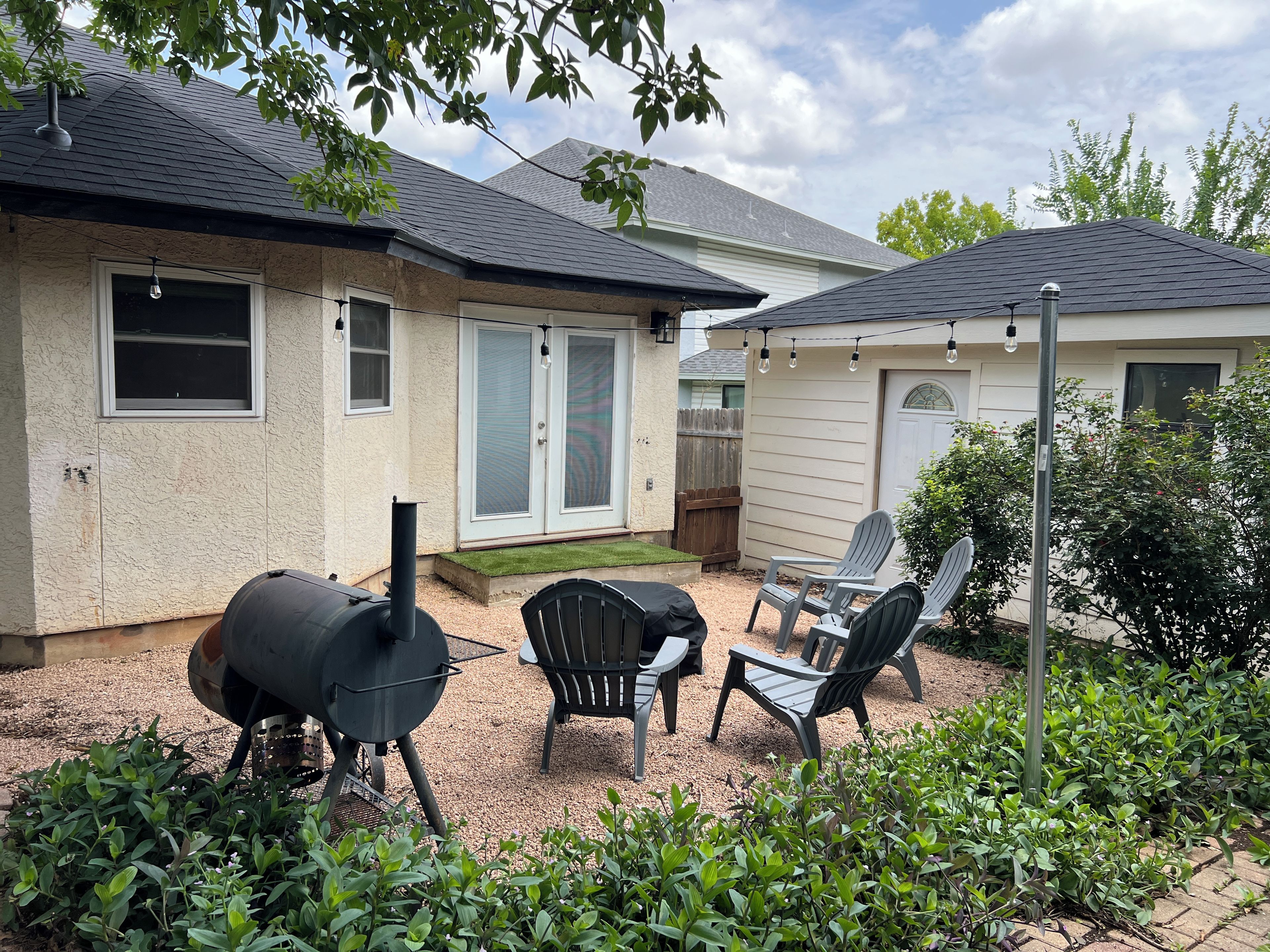 Een achtertuin met een barbecue, buitenzitplaatsen en een huis met een overdekt terras.