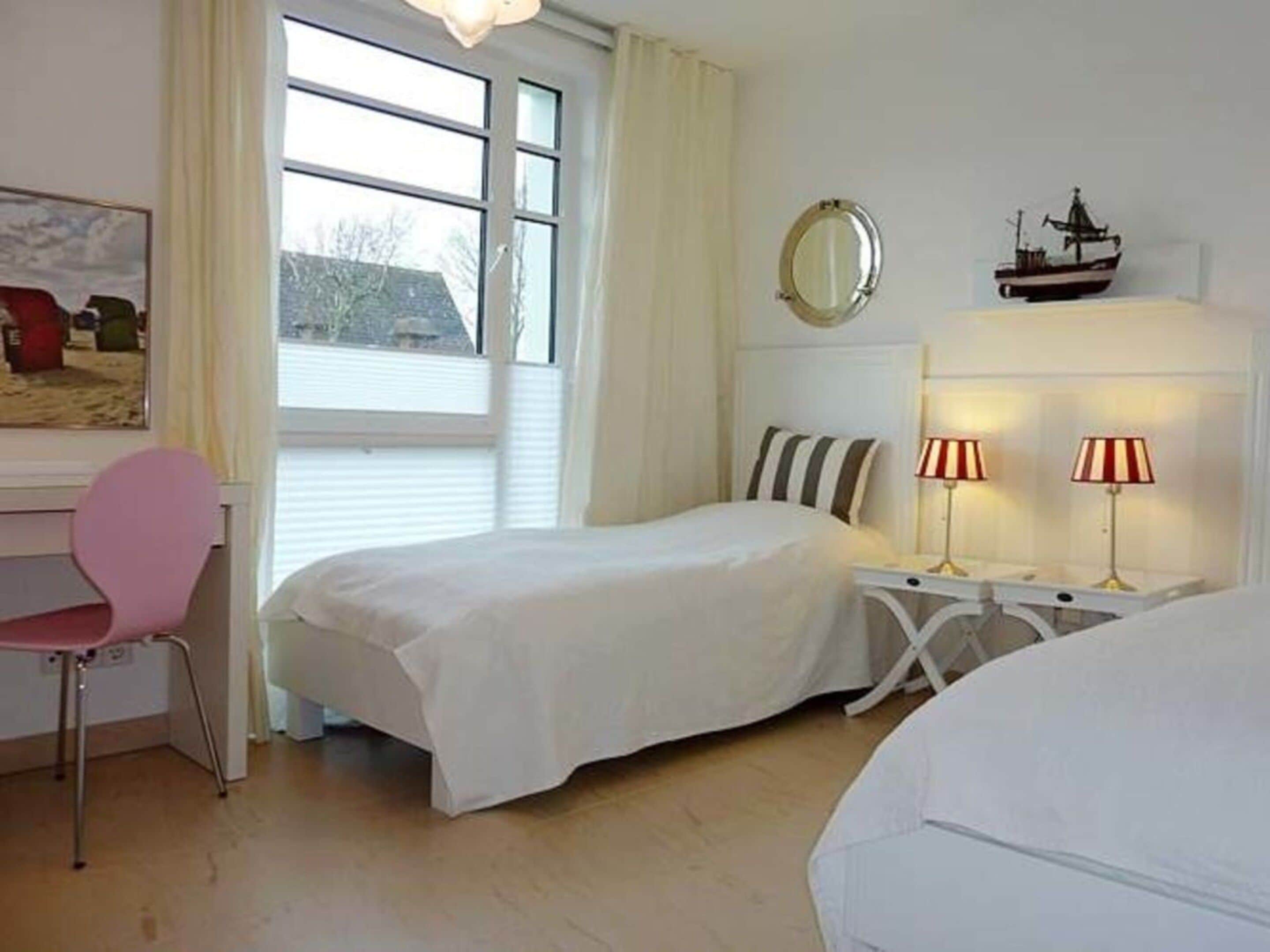 Een slaapkamer met een bed, bureau, stoel, raam en nachtkastje met lampen.