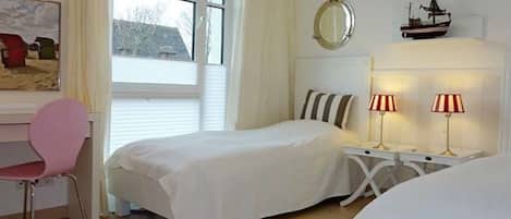 A bedroom with a bed, a desk, a chair, a window, and a bedside table with lamps.