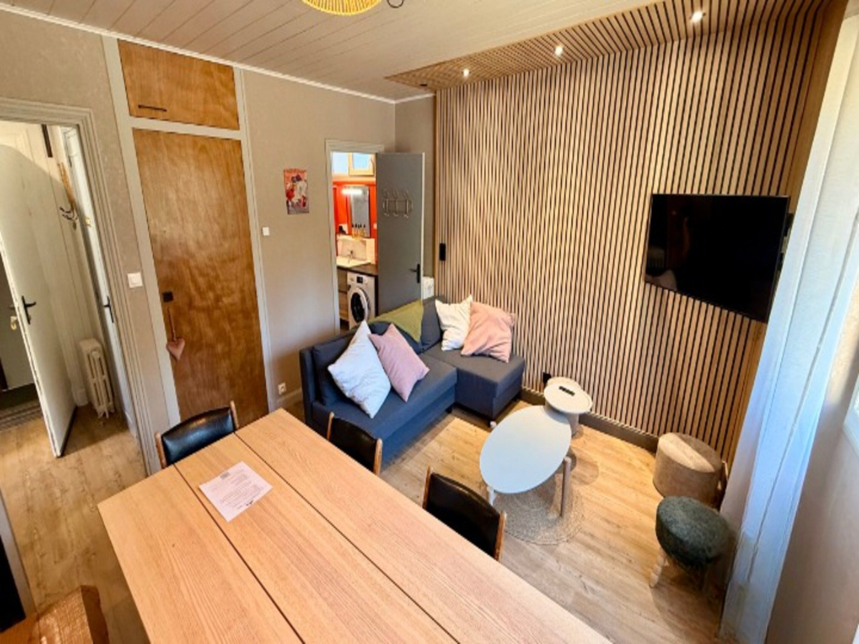 A modern living room with a sofa, a dining table, and a TV mounted on the wall.