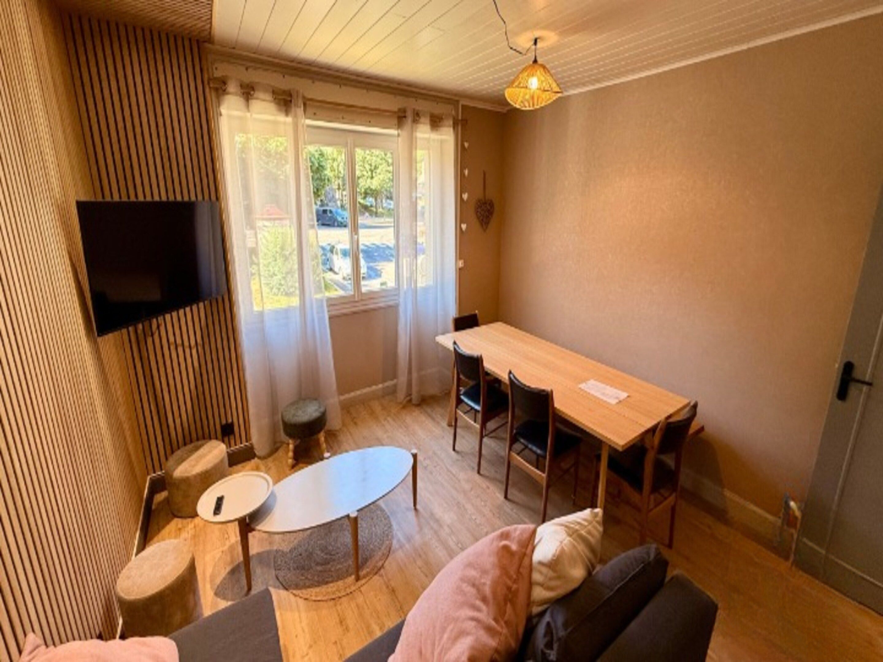 A room with a wooden floor, a sofa, a table, and a TV mounted on the wall.