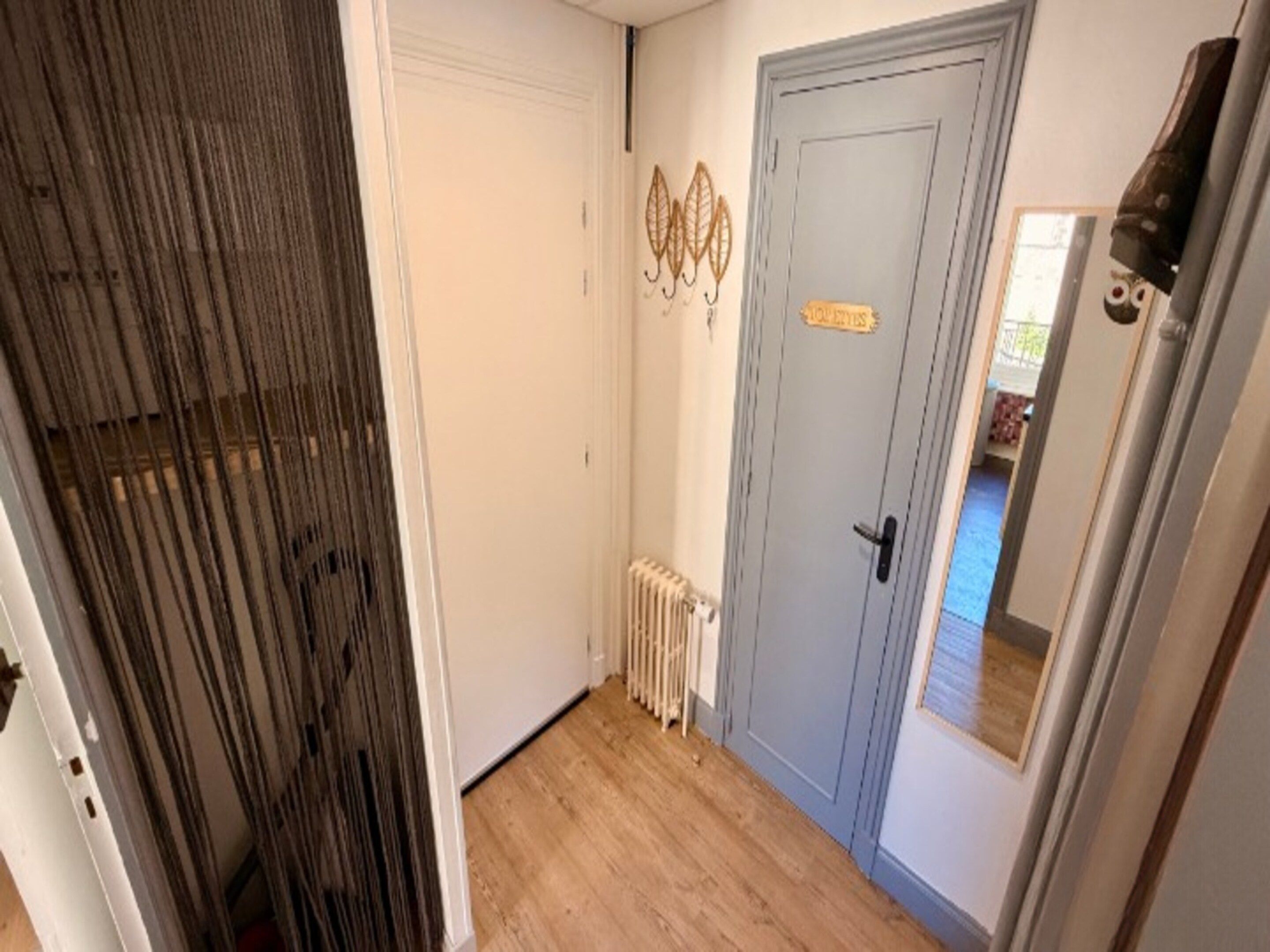 A hallway with a radiator, a door with a sign, and a mirror reflecting a room.