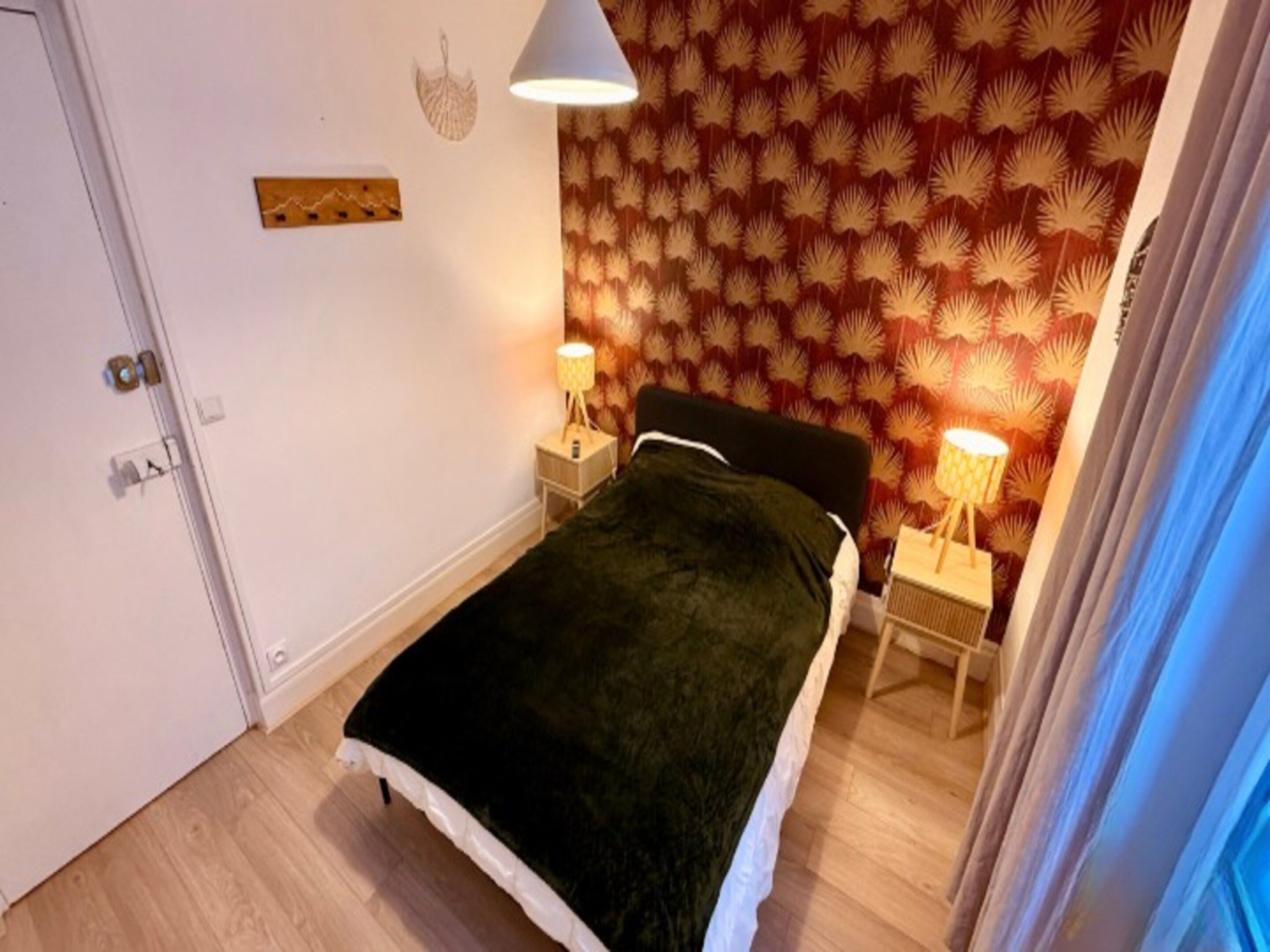 A bedroom with a bed, two bedside lamps, a door, and patterned wallpaper.