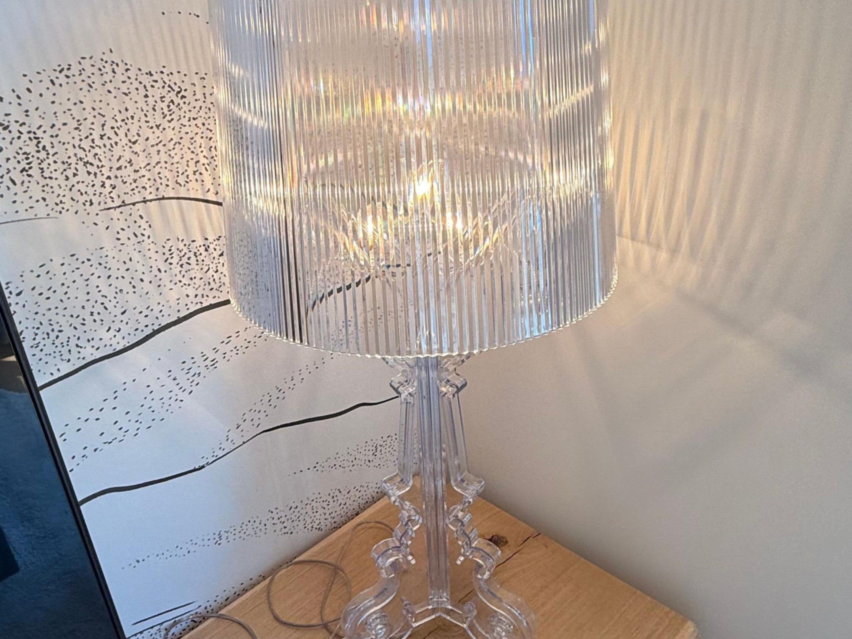 Een heldere glazen tafellamp met een gestreept kapje, op een houten ondergrond.