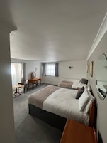 Habitación de hotel con una cama grande, un escritorio, una silla, una ventana con cortinas y un radiador.