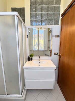 A bathroom with a shower enclosure, a sink with a mirror, and a wooden door. - 34a strada 1-bedroom  with AC in charming Lucca (Lucca)