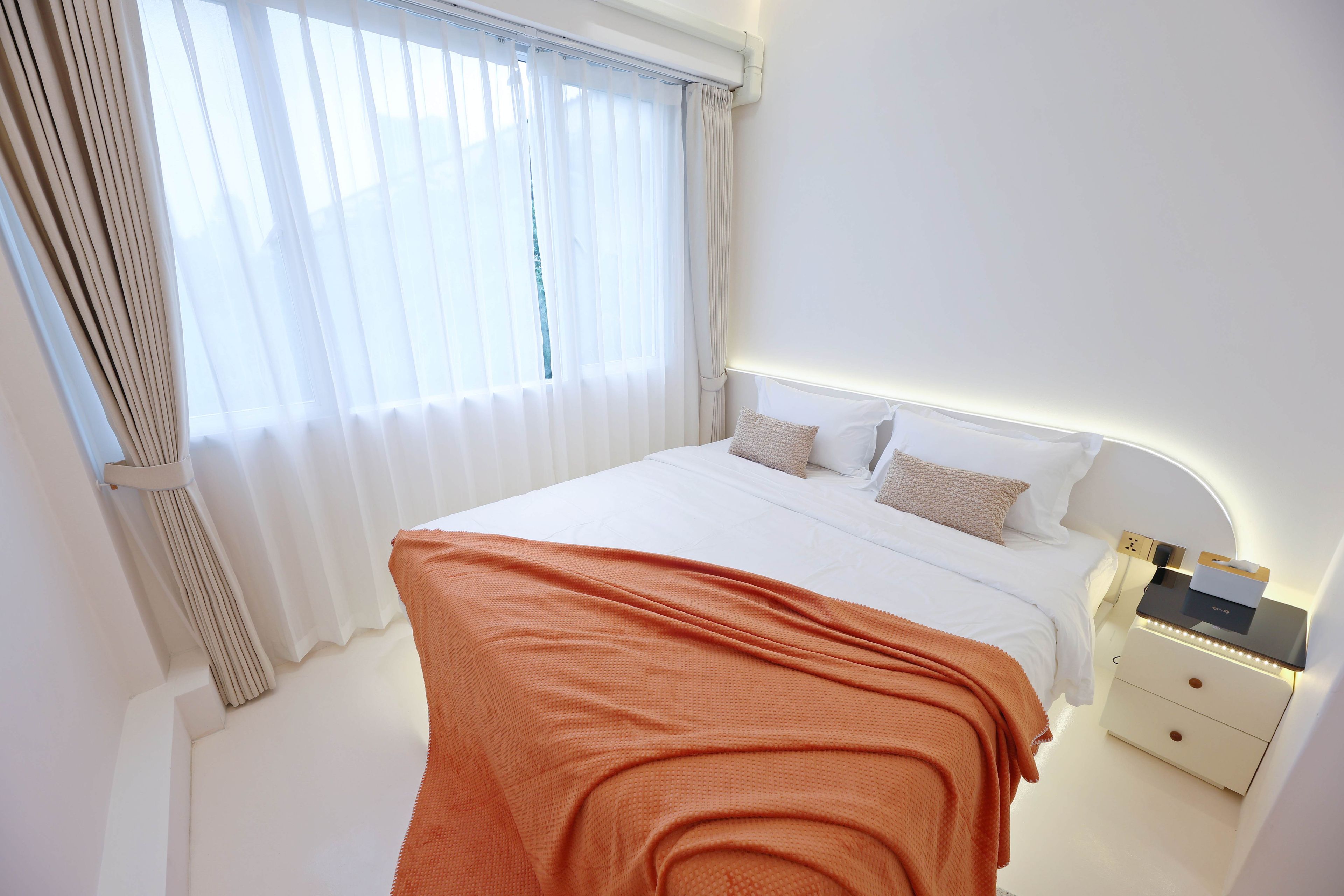Een hotelkamer met een bed, nachtkastje en een raam met gordijnen.