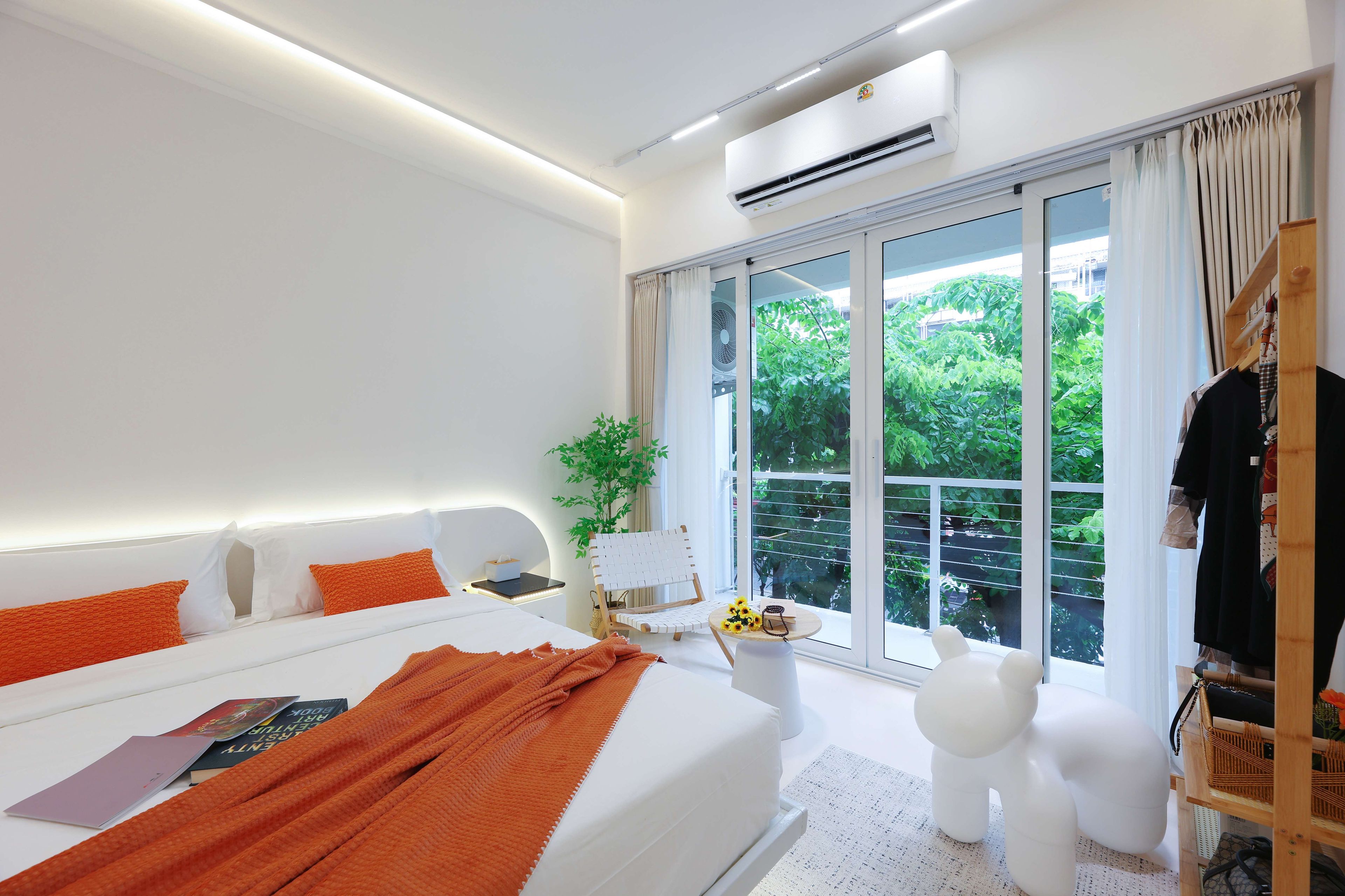 Une chambre moderne avec un grand lit, une table de chevet, une chaise, une petite table avec une plante et une armoire.