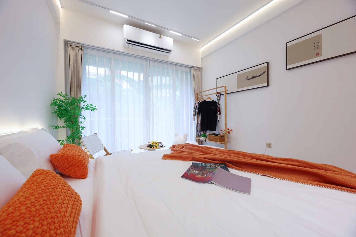Habitación de hotel con una cama grande, una mesita de noche, una planta en maceta, una ventana con cortinas y un aire acondicionado de pared.