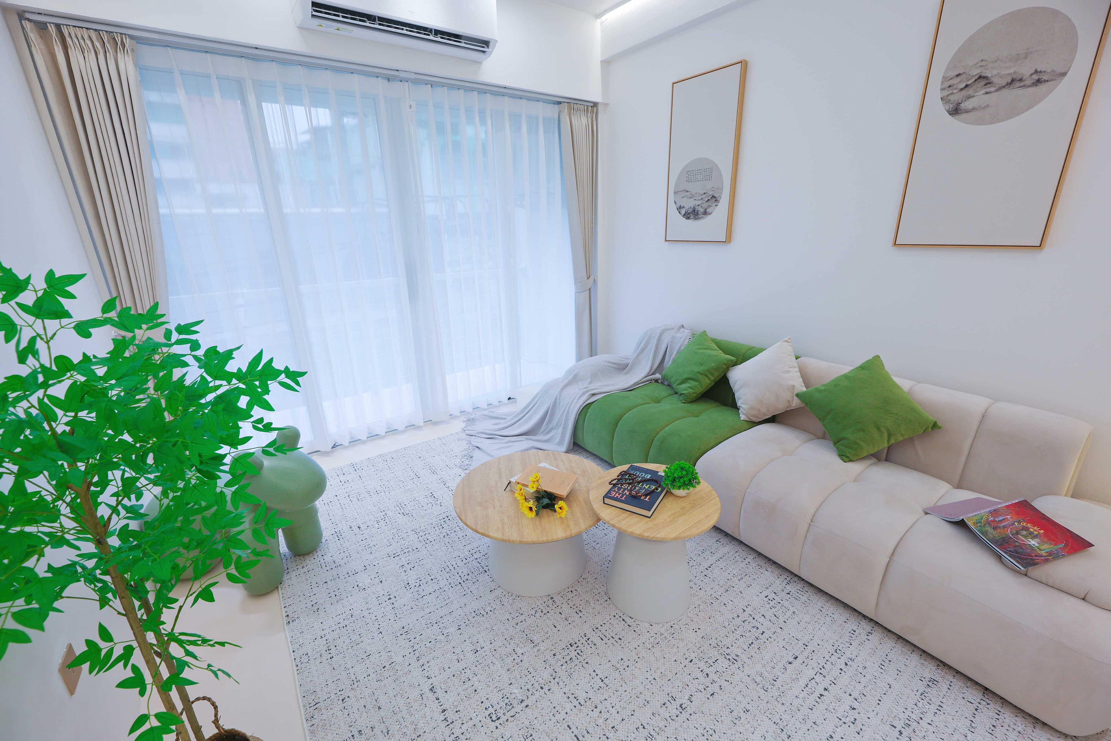 Un salon moderne avec un canapé, deux tables basses, une plante en pot et une grande fenêtre avec des rideaux.
