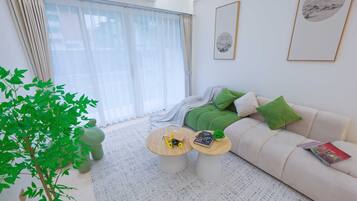 Un salon moderne avec un canapé, deux tables basses, une plante en pot et une grande fenêtre avec des rideaux.