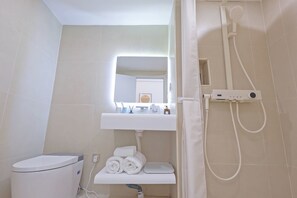Un baño moderno con inodoro, lavamanos, espejo y zona de ducha.