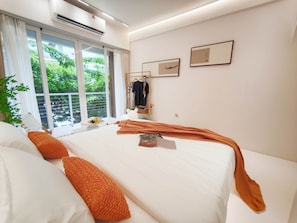 Un dormitorio moderno con una cama grande, una ventana con cortinas, un aire acondicionado de pared y una pequeña mesa con una planta.