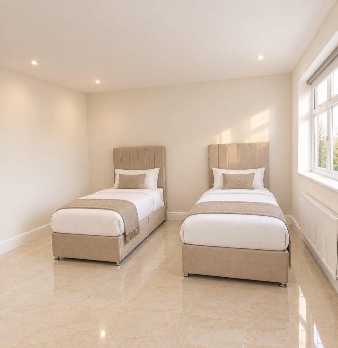 Une chambre d’hôtel avec deux lits, une grande fenêtre et un sol carrelé.