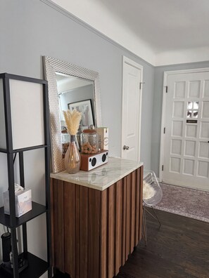 A room with a wooden vanity, a mirror, a shelf with decorative items, a door, and a chair. - Stylish 2-Bedroom, 2-Bath Private Fenced Home in Royal Oak (Royal Oak)
