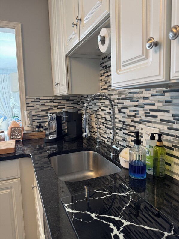 A modern kitchen with a black marble countertop, stainless steel sink, and a tiled backsplash. - Stylish 2-Bedroom, 2-Bath Private Fenced Home in Royal Oak (Royal Oak)