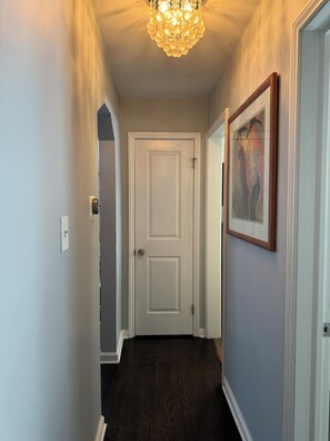 A hallway with a white door, a framed picture on the wall, and a chandelier. - Stylish 2-Bedroom, 2-Bath Private Fenced Home in Royal Oak (Royal Oak)