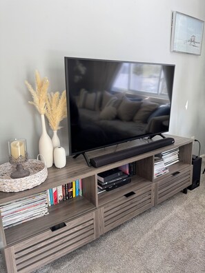 A flat-screen TV on a wooden entertainment center with a sofa, books, and decorative items. - Stylish 2-Bedroom, 2-Bath Private Fenced Home in Royal Oak (Royal Oak)