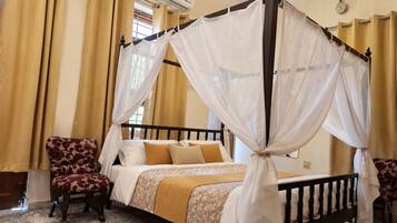 A four-poster canopy bed with a floral-patterned chair beside it, a second chair, and a carpeted floor.