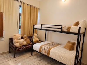 Een slaapkamer met een stapelbed, raam, gordijnen en een teddybeer.