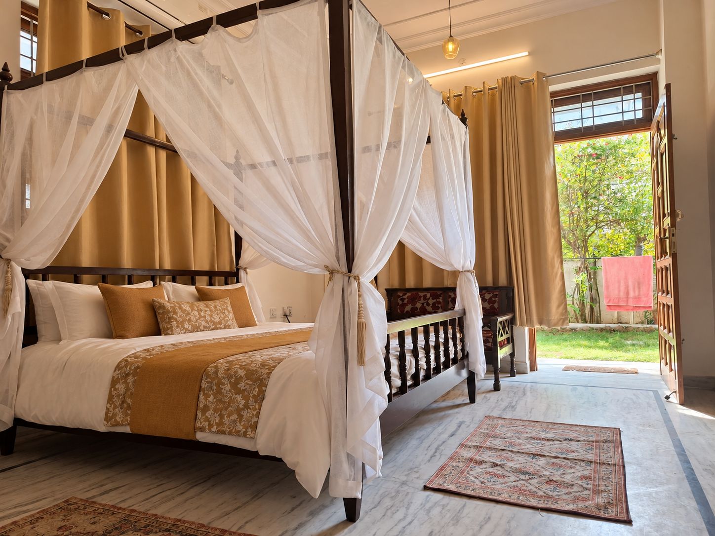 A four-poster bed with a canopy, a marble floor, and a view of a garden through an open door.