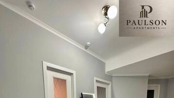 A hallway with white walls, a wooden floor, and doors with a diamond-patterned glass panel.