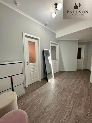 A hallway with white walls, a wooden floor, and doors with a diamond-patterned glass panel. - Brilliant 1-bedroom apartment with AC in charming Chișinău near  Airport. (Chișinău)