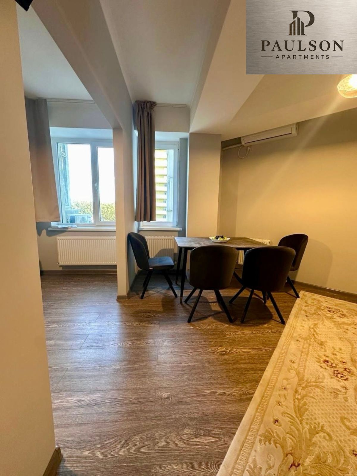 Un coin repas avec une table et des chaises, une fenêtre avec des rideaux et un radiateur.