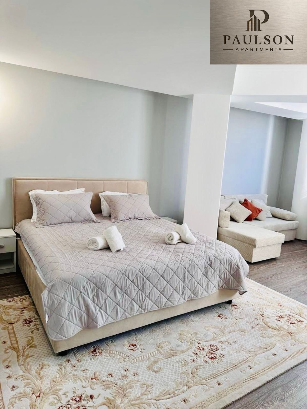 Une chambre à coucher avec un lit, des oreillers, une table de chevet, un canapé et un tapis à motifs.