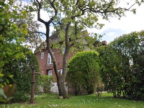 A red brick house with a white fence, surrounded by lush greenery and trees. - Old Registry Office Large Apartment (Oldsum)