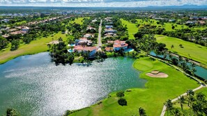 A golf course with a water body, surrounded by residential buildings and greenery. - Private Villa with Pool, Chef, and Golf Cart, Punta Cana (Punta Cana)